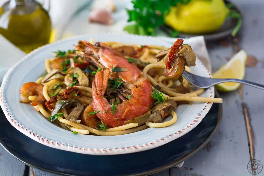 primo con carciofi e gamberi in un piatto azzurro e decorazioni sul tavolo